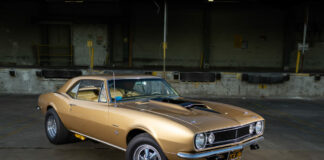 001 A golden 1967 Camaro with black stripes parked in an industrial warehouse