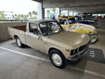 21 Beige vintage chevy luv pickup with wear marks parked in a garage next to a colorful classic car