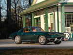 03 1966 Chevrolet Corvette Stingray in dark green bathed in daylight parked near a retro themed shop