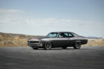 001 A side profile of a 1971 Chevrolet Nova with dark gray paint aftermarket wheels and a lowered stance on an open road