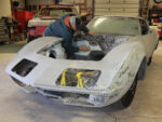 01 A 1971 Corvette undergoing bodywork restoration with a person sanding the engine bay