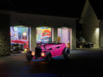 03 1932 Ford Roadster in a driveway showcasing a garage filled with vintage cars and signs