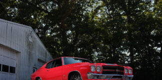 001 Red 1970 Chevrolet Chevelle SS with black racing stripes parked in front of a vintage garage
