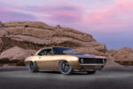 003 Side angle of a sleek 1969 Chevy Camaro in gold with a black hood set against desert rock formations