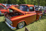 09 1957 Chevrolet Pickup in metallic orange customized with a lowered stance and chrome wheels drawing attention at the car show