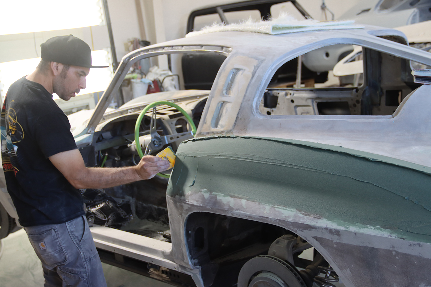 13 Restoration specialist applying body filler to the rear quarter panel of a C2 Corvette for a seamless finish