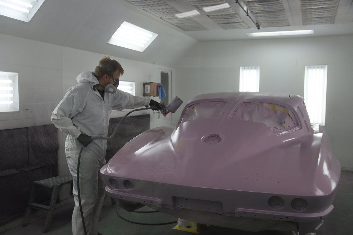 21 C2 Corvette receiving a fresh coat of primer in a professional paint booth during the restoration process