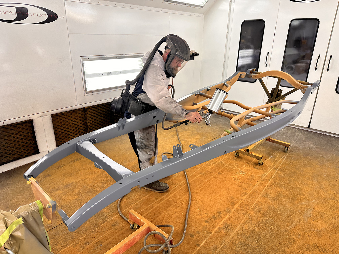 05 Technician spraying a roadster frame with gray primer in a professional paint booth