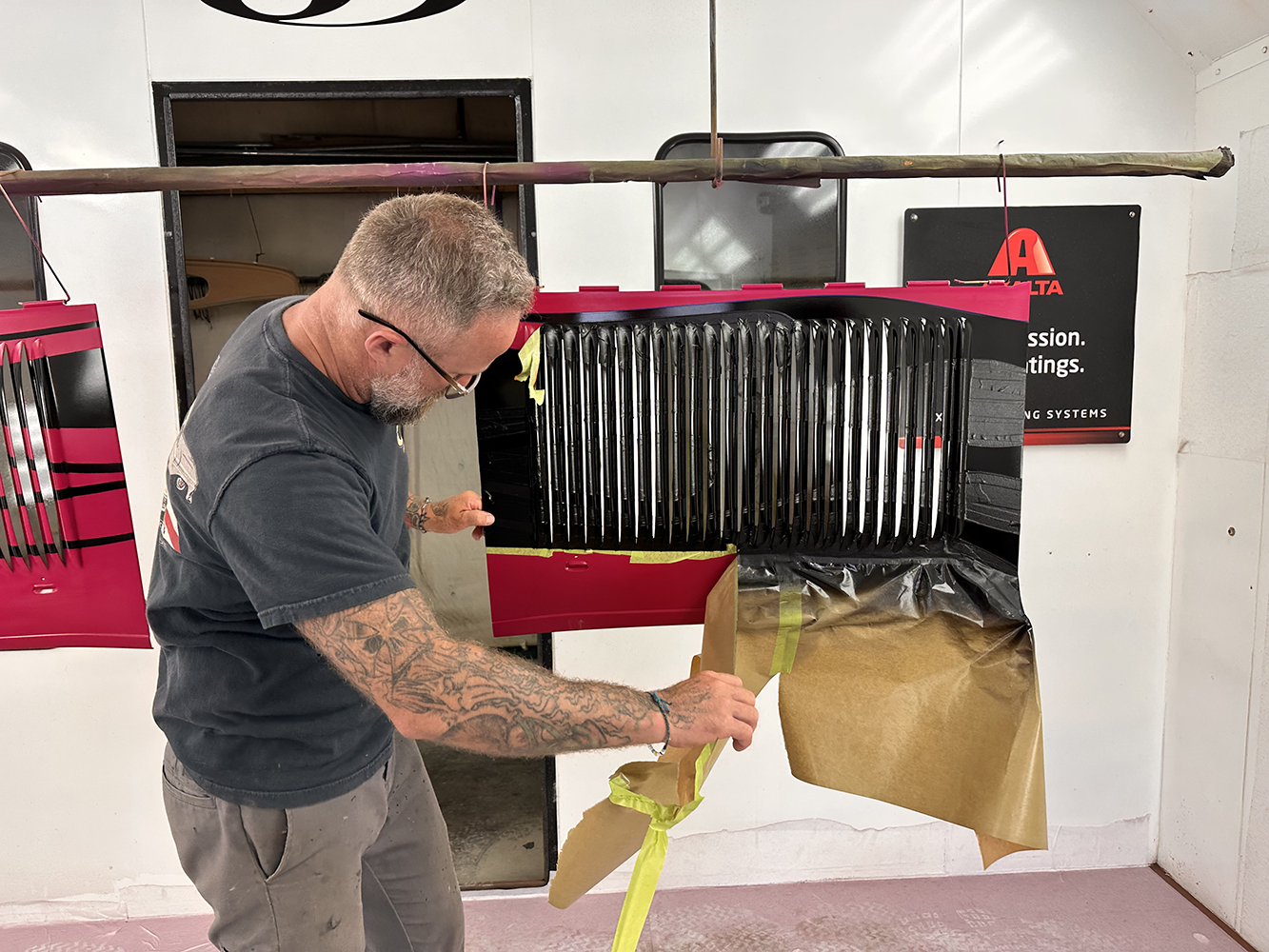 19 Painter peeling masking tape to reveal sharp black flame patterns on the roadster’s hood