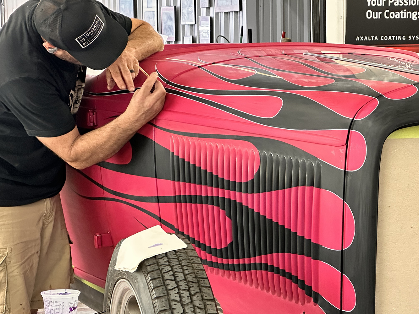 24 Artist adding white pinstriping details to outline black flames on the roadster s pink body