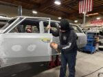 001 Technician sanding door panel gaps in a restoration shop with an orbital sander