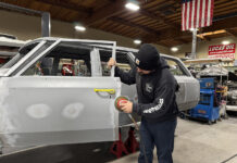 001 Technician sanding door panel gaps in a restoration shop with an orbital sander