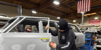 001 Technician sanding door panel gaps in a restoration shop with an orbital sander