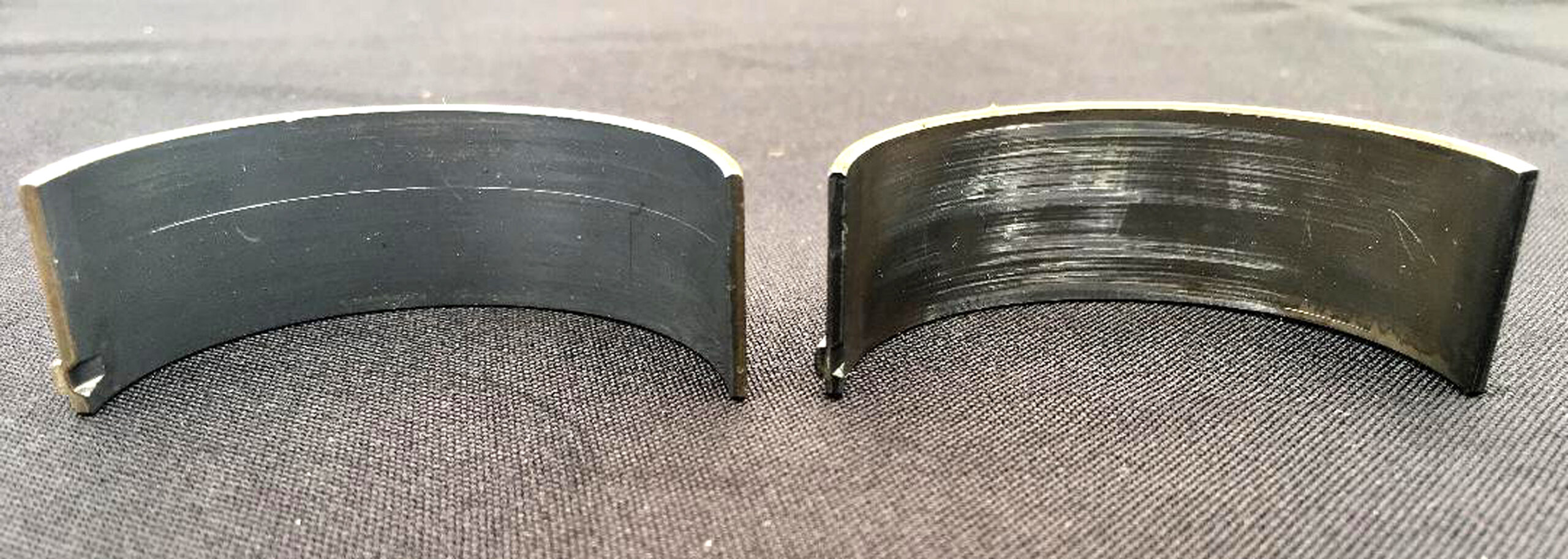 002 Side by side comparison of worn and damaged engine bearing surfaces on black background