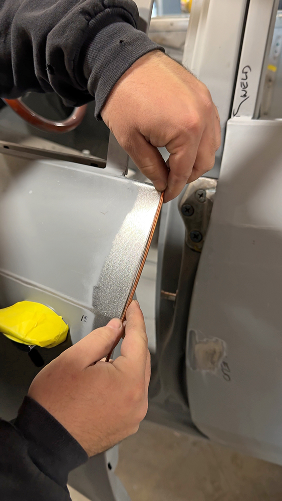 003 Technician positioning a thin copper strip between door edges for gap uniformity