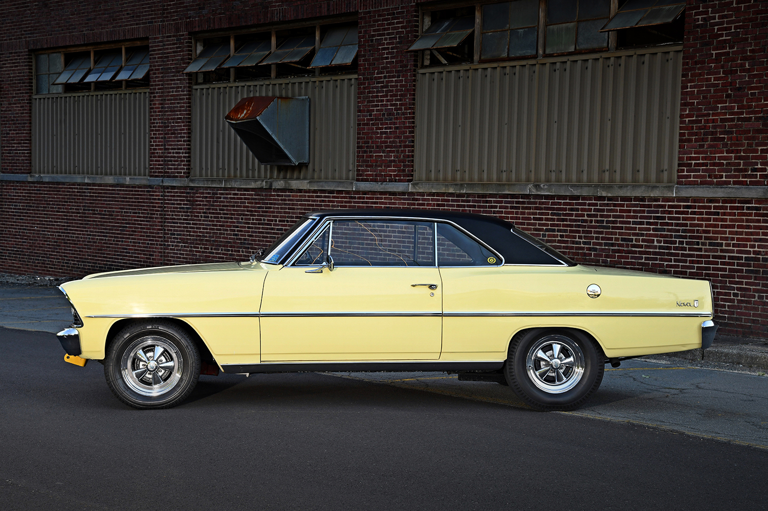 004 1967 Chevrolet Nova SS in yellow with black vinyl top chrome Cragar wheels parked by industrial brick walls