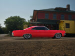 005 1965 Chevrolet Impala SS red side profile view lowered stance custom wheels against vintage train station background