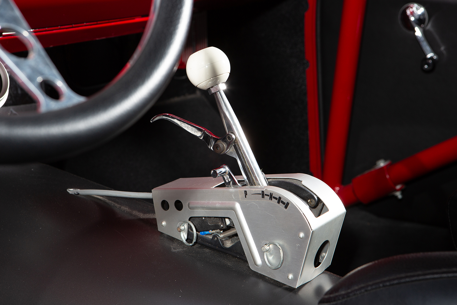 012 1957 Chevrolet Bel Air Hurst shifter with a white ball knob and ratchet style mechanism mounted in a custom aluminum housing