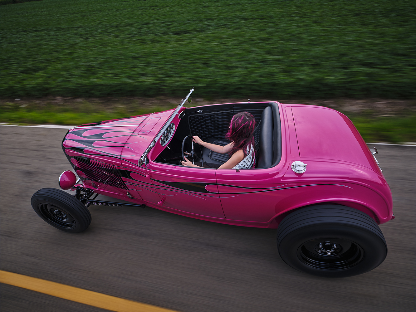 21 Vibrant pink 1932 Ford Roadster with black flames captured in motion with a driver on an open road