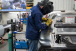 00 technician welding the new quarter panel onto the car using a Miller welder for precision attachment