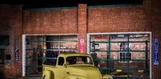 01 1952 Chevrolet 3100 parked at a vintage gas station with a sleek olive green paint job and chrome grille