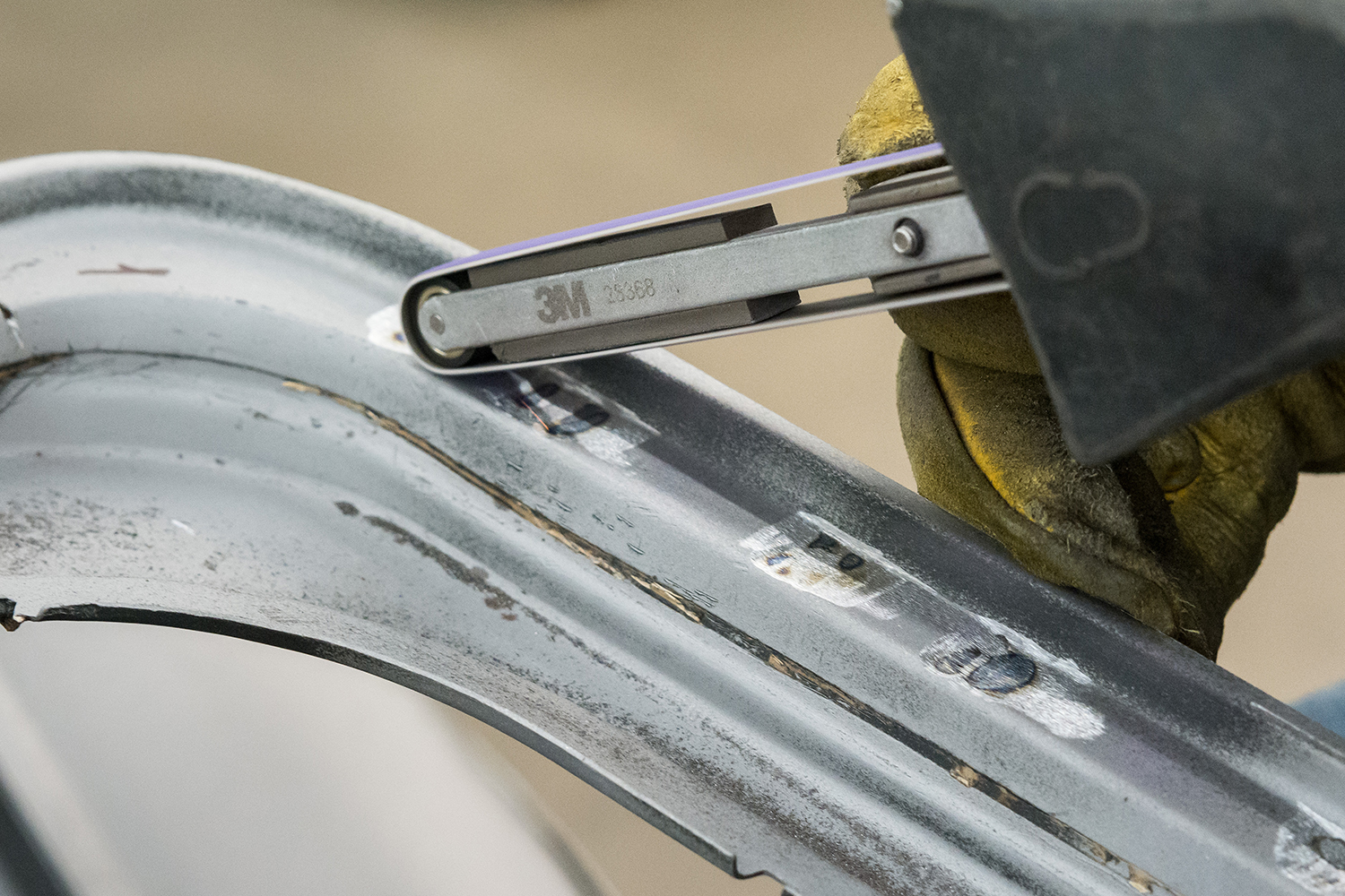 08 technician using a 3M belt sander to clean the mounting surface before welding the new panel