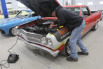 000 1965 Chevrolet El Camino with custom flames undergoing electrical repair in a classic car garage