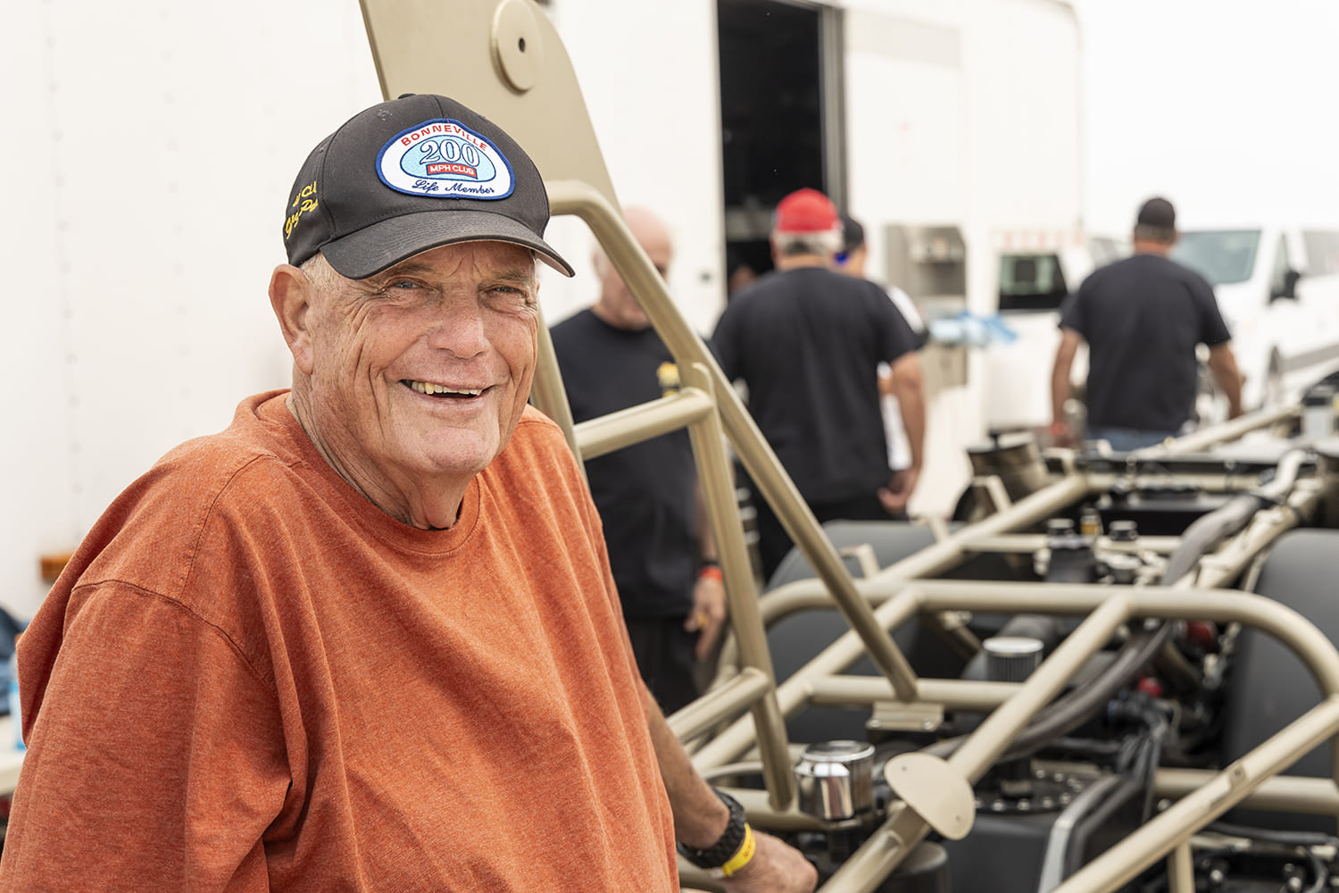 21 George Poteet wearing Bonneville 200 MPH Club hat beside land speed race car chassis at dry lakes event