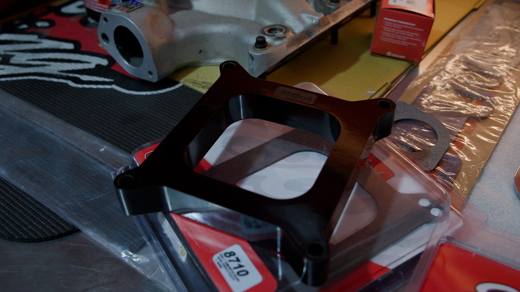 18 Edelbrock 8710 4 hole spacer with laser etched logo shown alongside gaskets and hardware