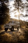 44 1959 Chevrolet Apache lifted 4x4 with overland camper shown off road under golden sunlight in scenic forest backdrop