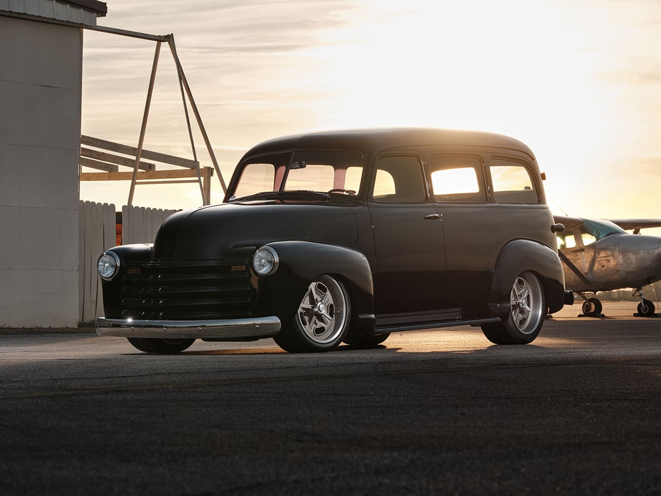 03 1952 Chevy Suburban black low front passenger view modern wheels hangar and fence