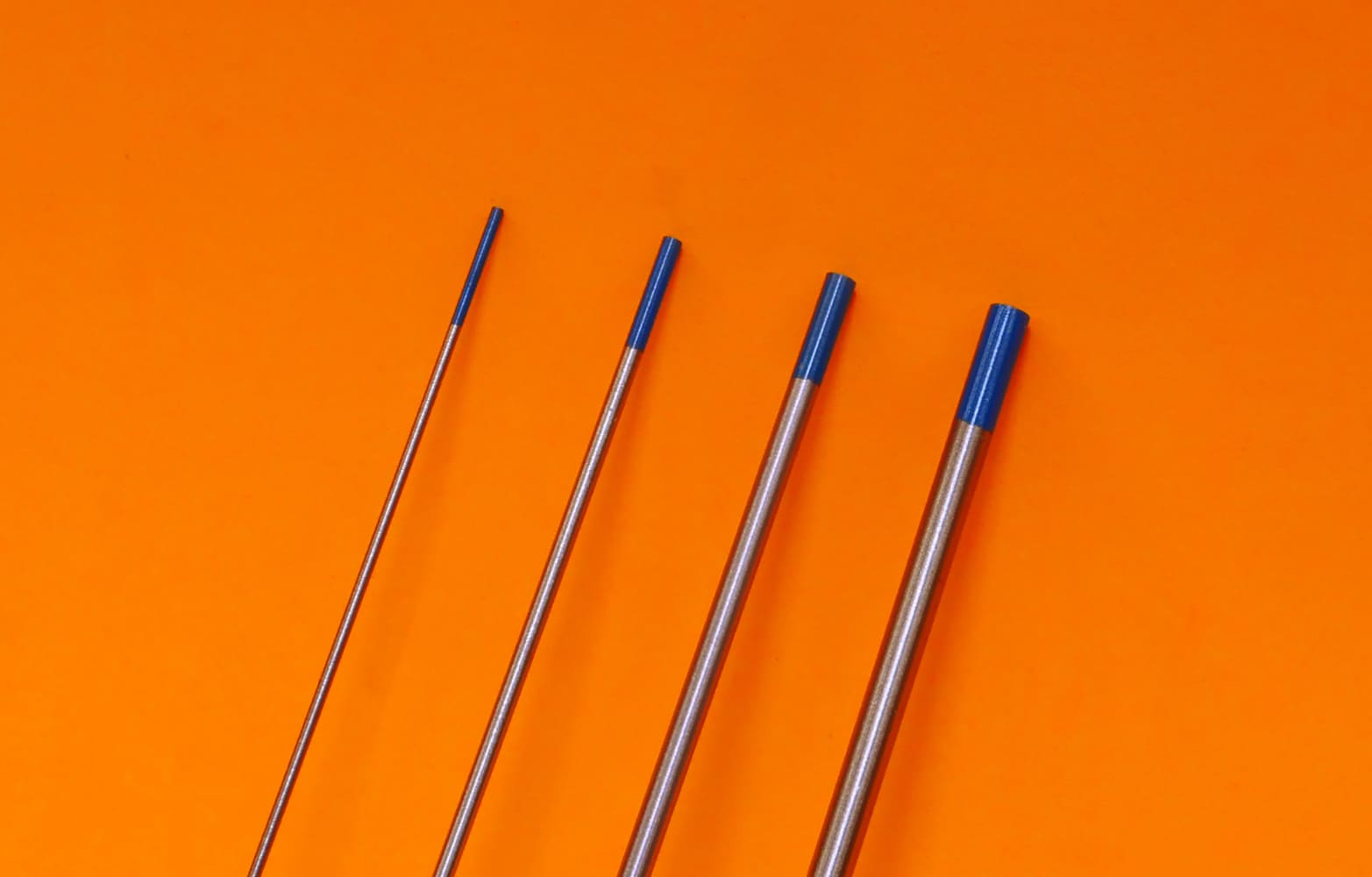 04 Four TIG electrodes blue tips mixed diameters aligned on orange backdrop