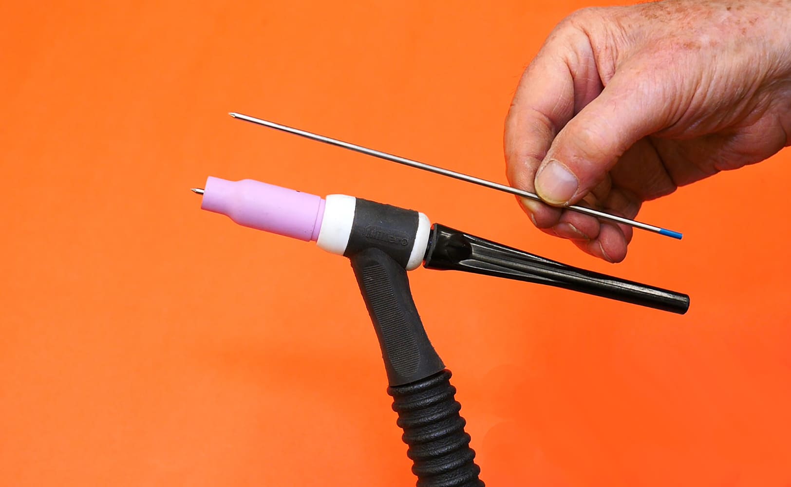 05 TIG torch holding blue tip tungsten pink cup operator positioning electrode orange background