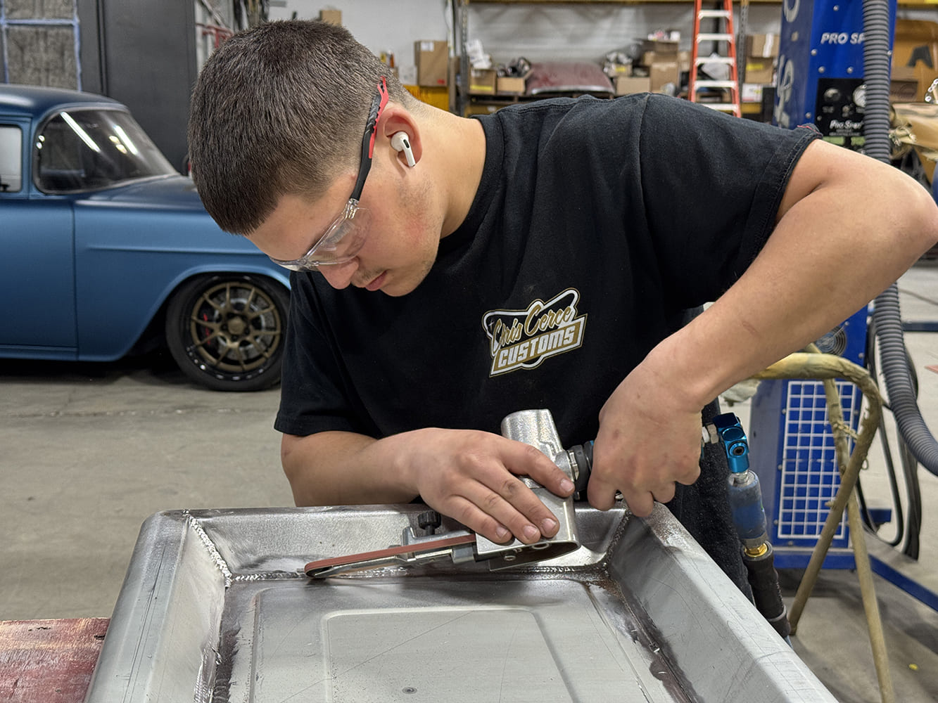 01 Tech working tailgate edge air tool in hand safety gear Club Carce Customs shirt blue classic pickup in background