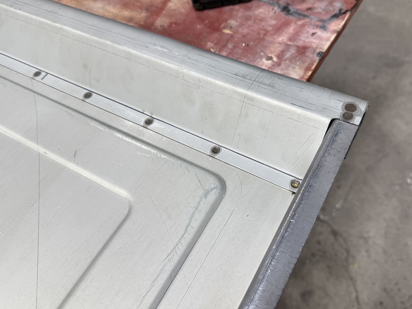 03 Tailgate edge close up evenly drilled holes in reinforcement strip clean welds surface scratches mallet partially visible