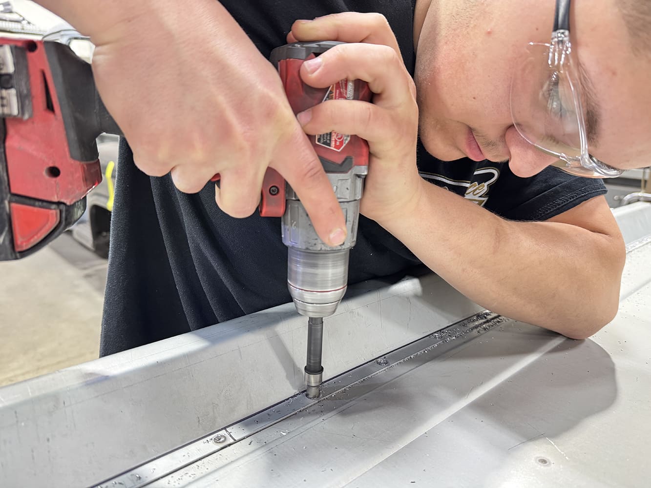 05 Red Milwaukee impact driver on strip fastenersspot weld heads visible operator in ear protection Club Carce Customs tee