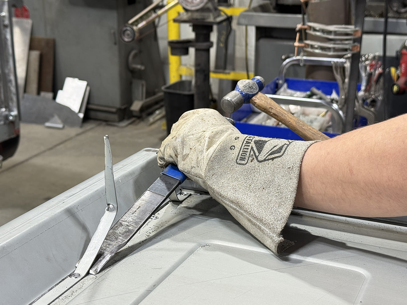 08 Blue handled panel separator on seam gloved hand hammer nearby shop equipment in background