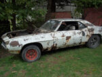020 1969 Chevrolet Camaro heavily rusted side view project car with mismatched wheels and missing hood