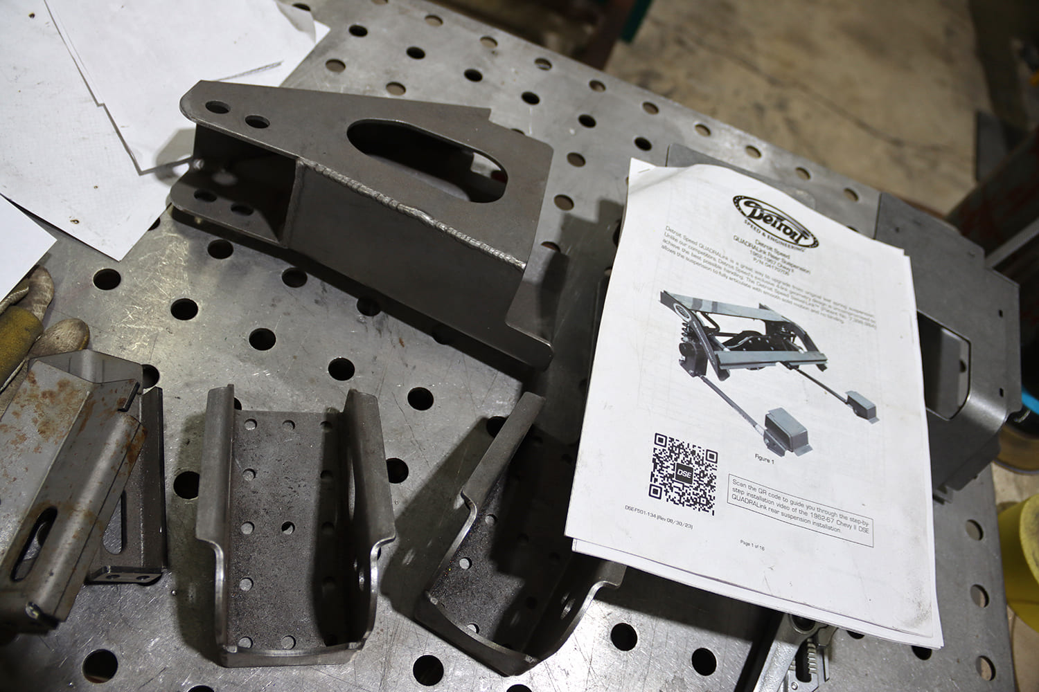 003 1963 Chevy Nova Detroit Speed QUADRALink kit parts and installation manual staged on a fab table
