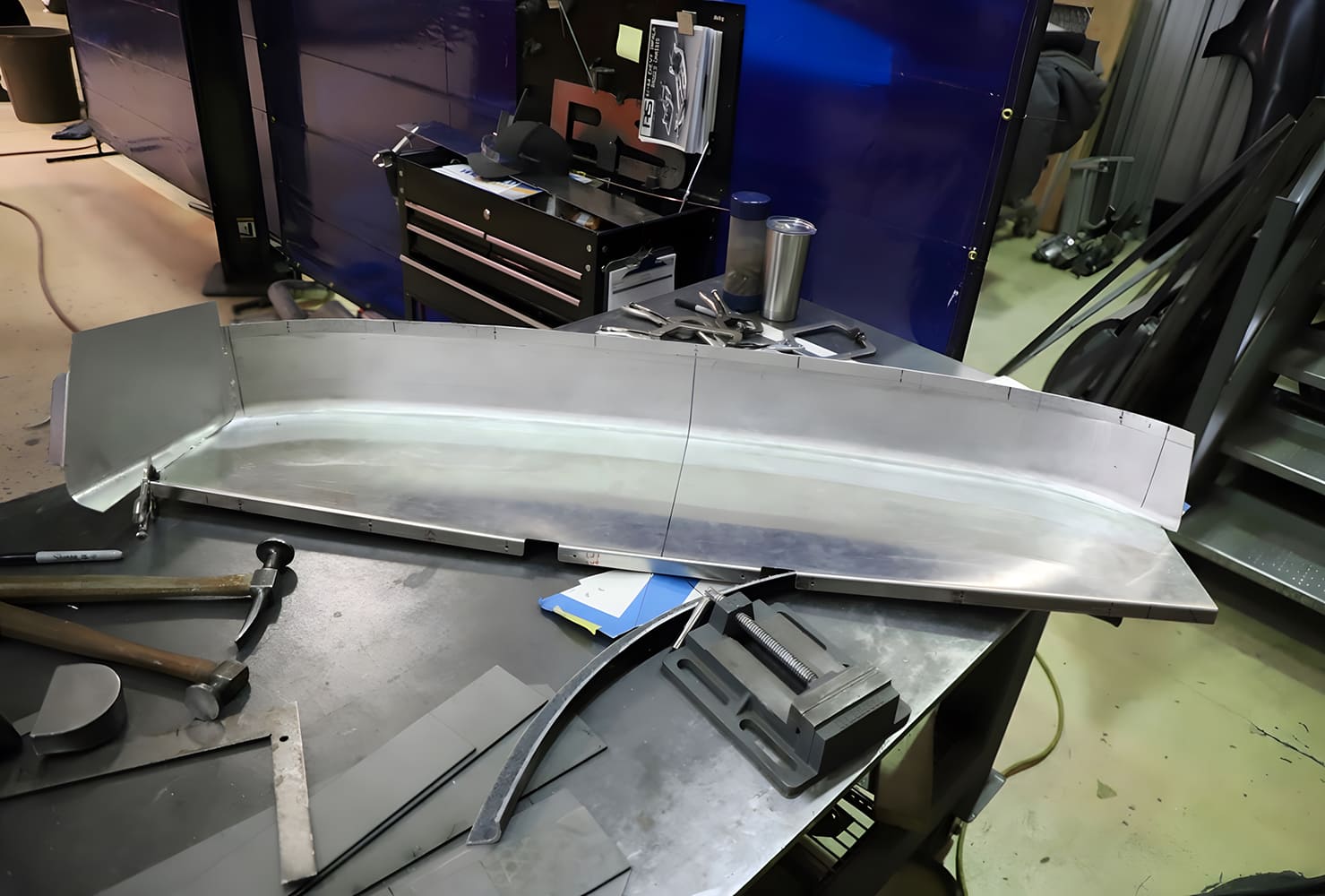Raw aluminum rear panel in fabrication with hammer form tools nearby