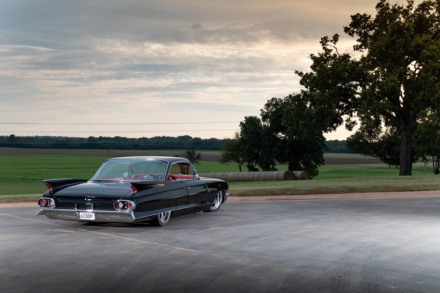 1961 Cadillac Coupe DeVille black custom lowrider rear three quarter view tailfins chrome bumper countryside setting