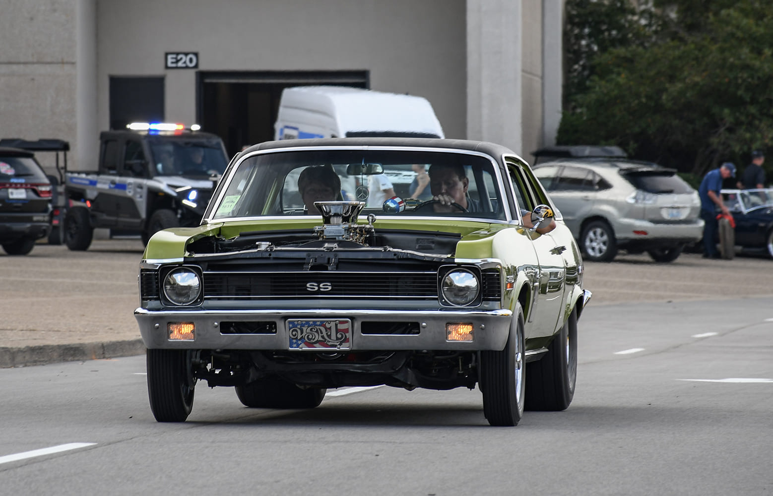 Front three-quarter view of an orange 1969 Chevy Nova SS Pro Street car with an open hood, roll cage, and large rear drag slicks.