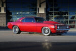 Low-angle side profile view of a candy apple red metallic 1969 Chevy Camaro restomod parked on concrete, featuring a cowl induction hood, polished deep-dish wheels, and tinted windows.