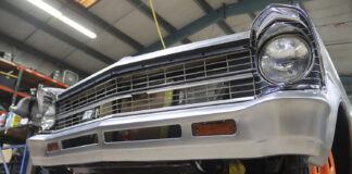 Low-angle front view of a second-generation Chevy Nova featuring a custom-fabricated, brushed steel reshaped front bumper and lower valance with integrated turn signals in a shop.