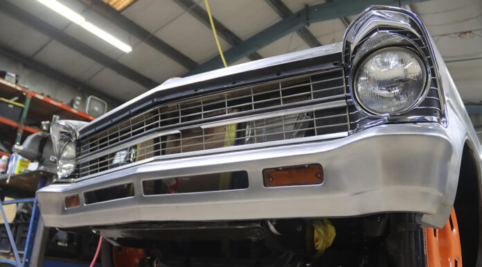 Low-angle front view of a second-generation Chevy Nova featuring a custom-fabricated, brushed steel reshaped front bumper and lower valance with integrated turn signals in a shop.