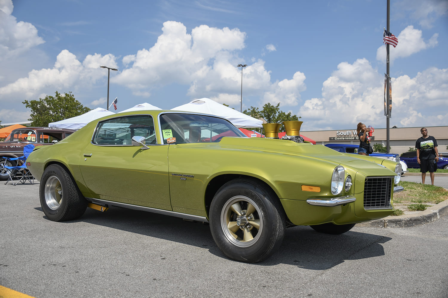 Side profile of an olive green second-generation Chevy Camaro featuring gold dual velocity stacks rising above a custom cowl hood.