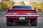 Full side profile view of a candy apple red metallic 1969 Chevy Camaro coupe featuring a low pro-touring stance, cowl induction hood, tinted glass, and large polished multi-spoke wheels.