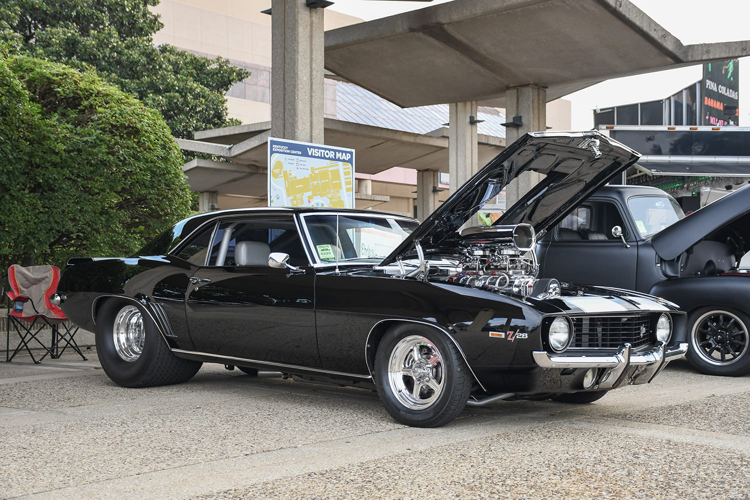 Front three-quarter view of a black 1969 Chevrolet Camaro Z/28 with an open hood displaying a supercharged engine with a polished bug catcher scoop and massive rear drag slicks.