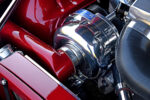 Detailed close-up of a polished ProCharger centrifugal supercharger unit with custom candy red boost piping and black silicone coupler in a 1969 Chevy Camaro engine bay.