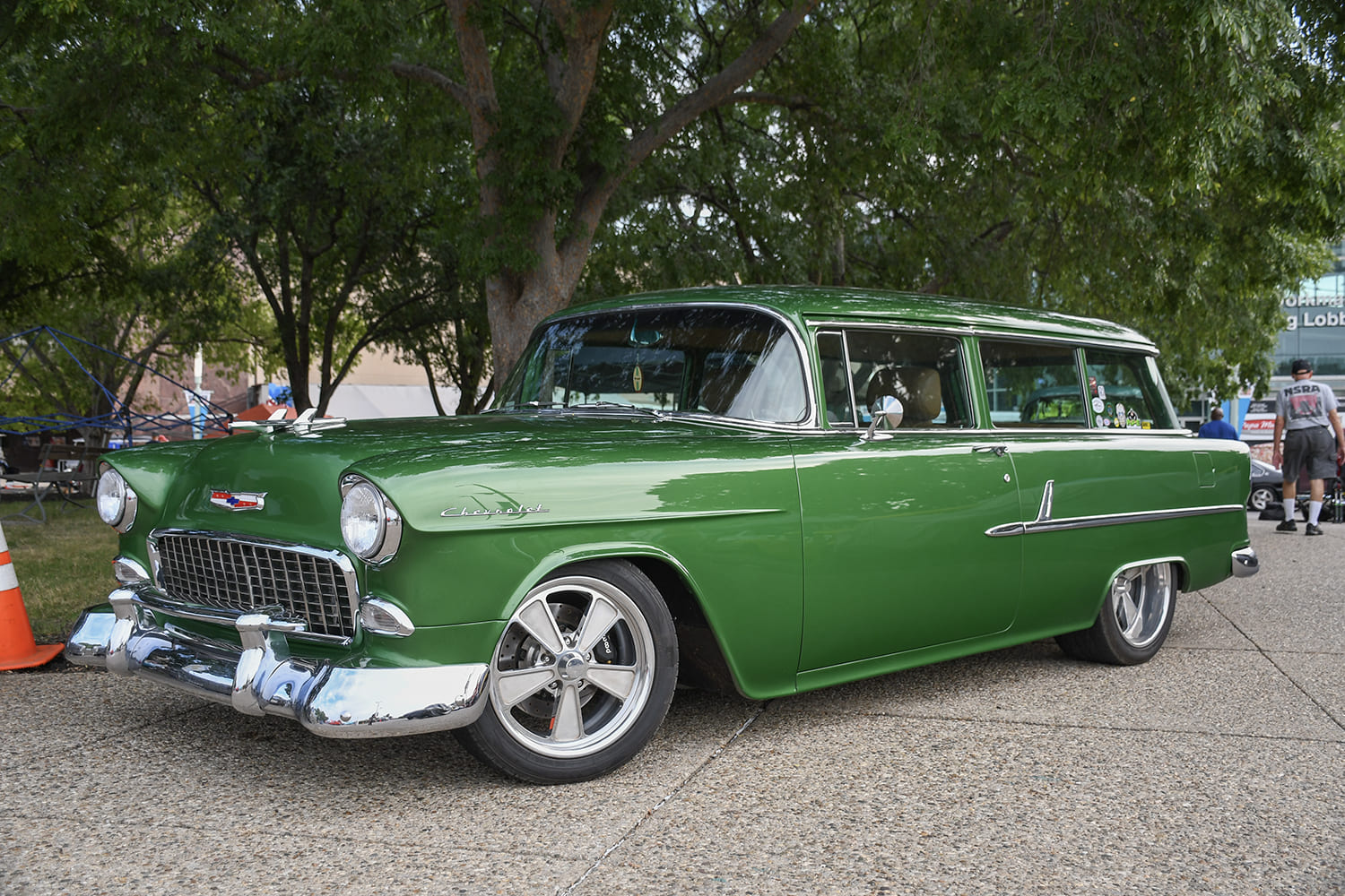 Front three-quarter low angle of an olive metallic green 1955 Chevrolet two-door Handyman station wagon with modern five-spoke wheels and chrome trim.